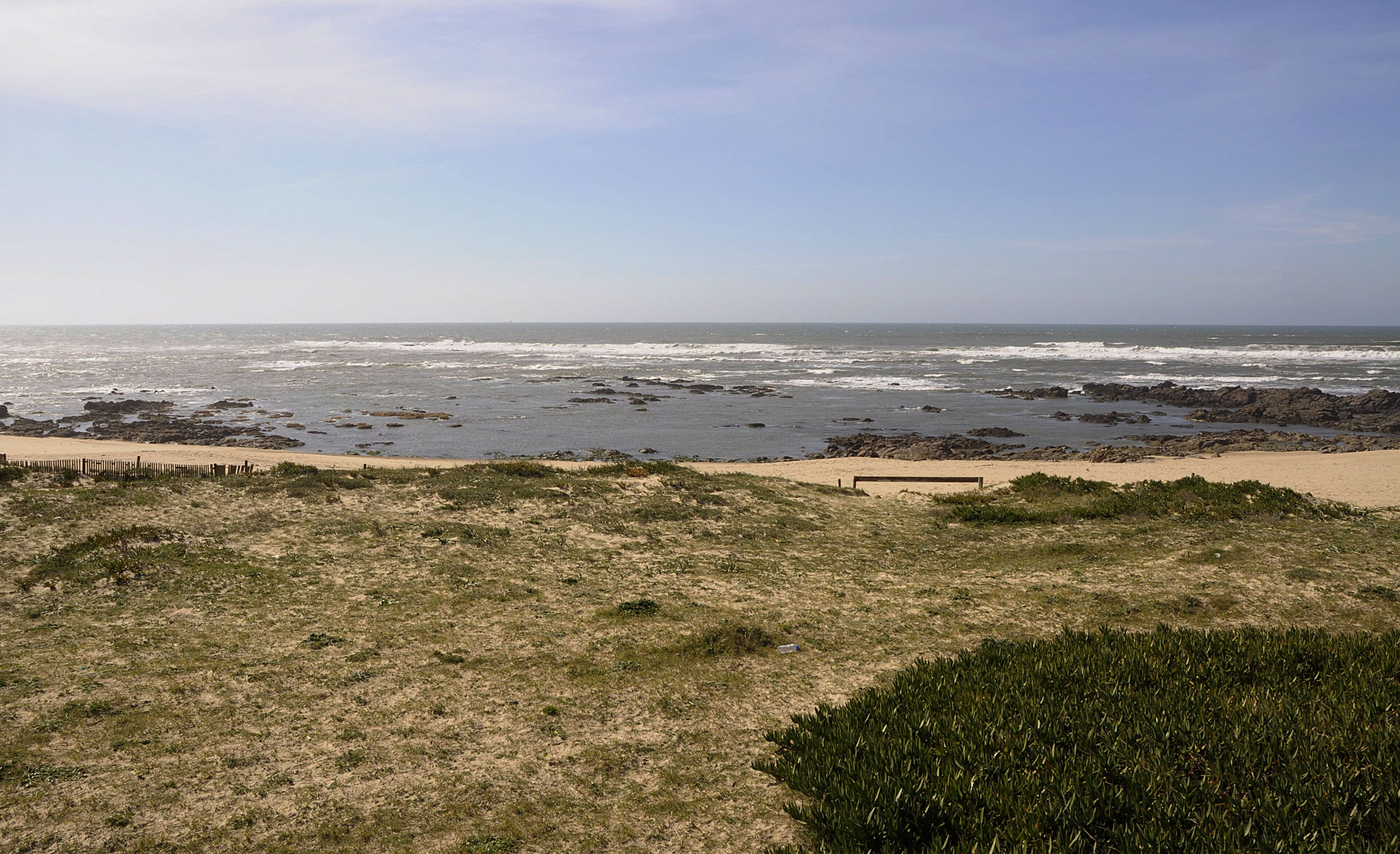 Una playa con costa rocosa, arena y vegetación escasa.