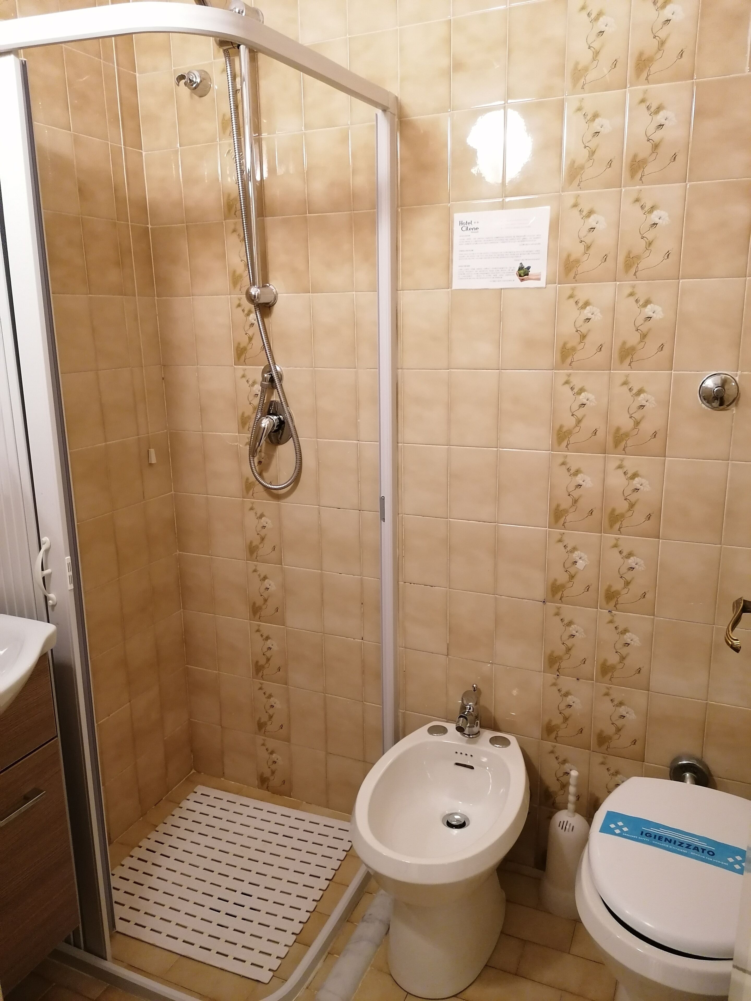 A bathroom with beige tiles, a shower, a sink, and a toilet.
