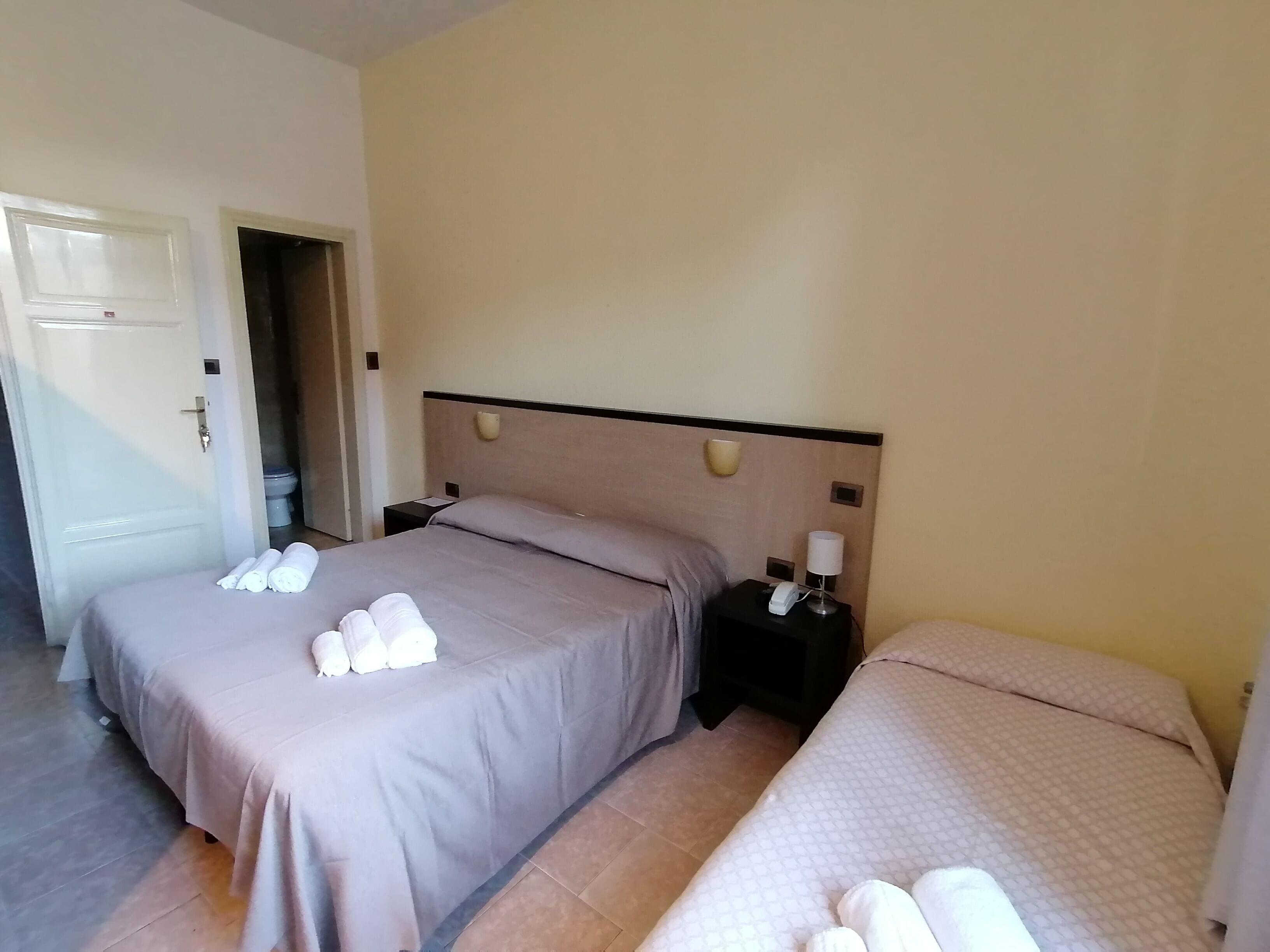 A hotel room with two beds, each with a headboard, a nightstand, and a lamp.