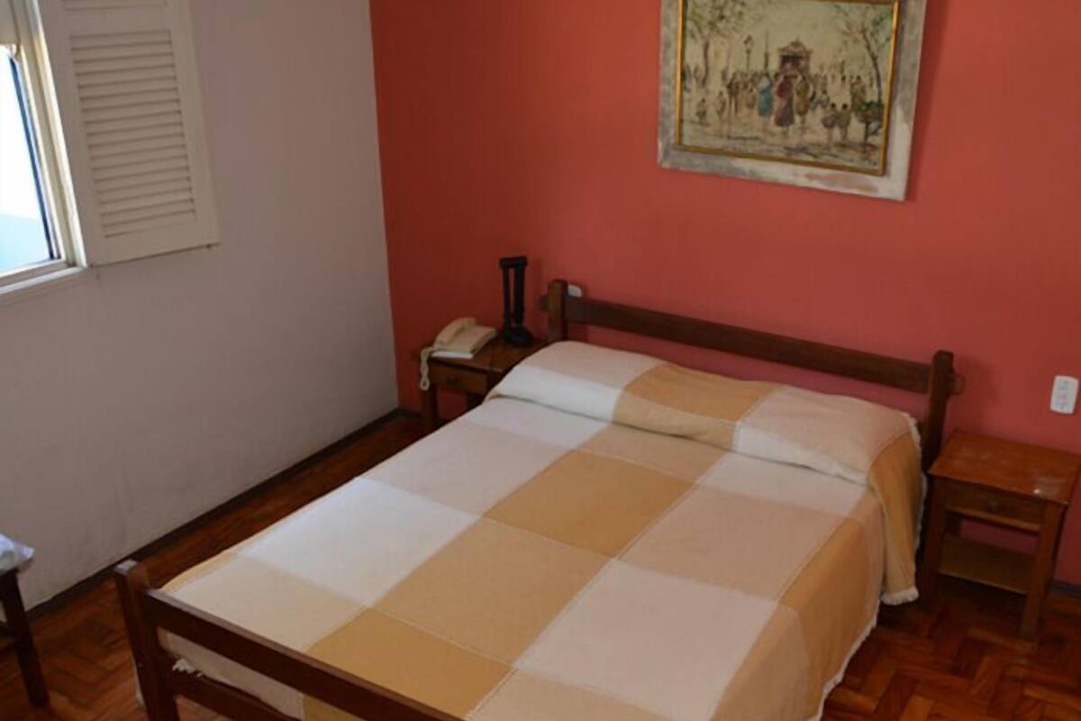 A bedroom with a wooden bed, a nightstand, a telephone, and a painting on the wall.