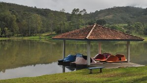 A gazebo with a tiled roof by a calm lake, surrounded by lush greenery and hills. - Hotel Termópolis (Sao Sebastiao do Paraiso)