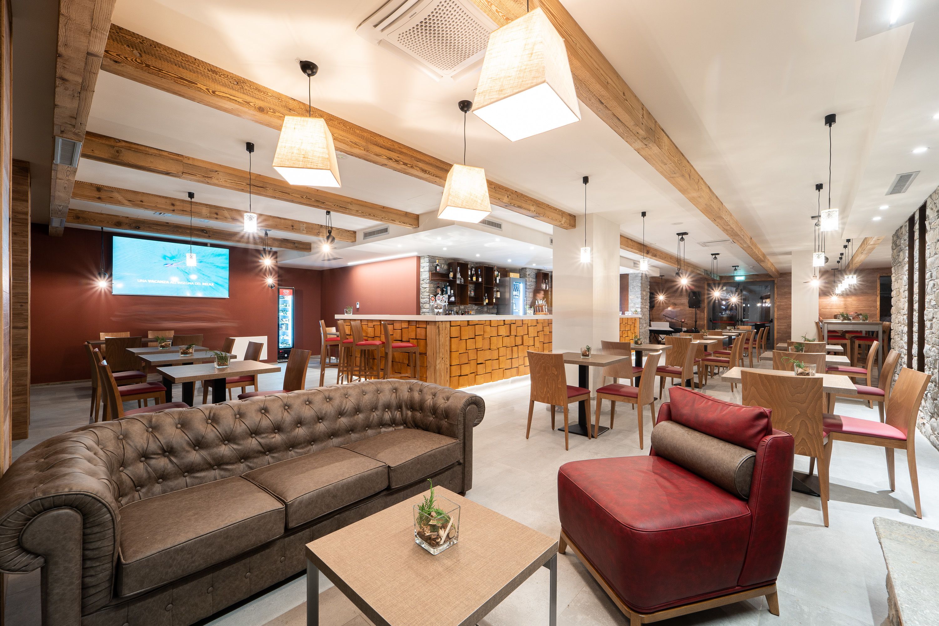 Un grand espace intérieur comprenant un bar, des coins salon et un écran de télévision.
