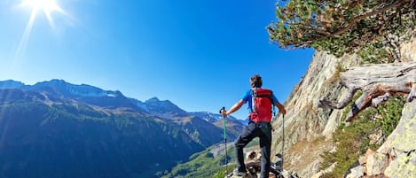 Un excursionista en un sendero montañoso y pedregoso con vistas despejadas de un valle y montañas distantes.