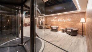 A modern lobby with a wooden wall, a sign reading "Welcome to IT family world," and a seating area with two sofas and a lamp. - TH Courmayeur (Courmayeur)