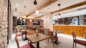 Un restaurante con mesas y sillas de madera, una pared de piedra y una zona de bar con estantes llenos de botellas.