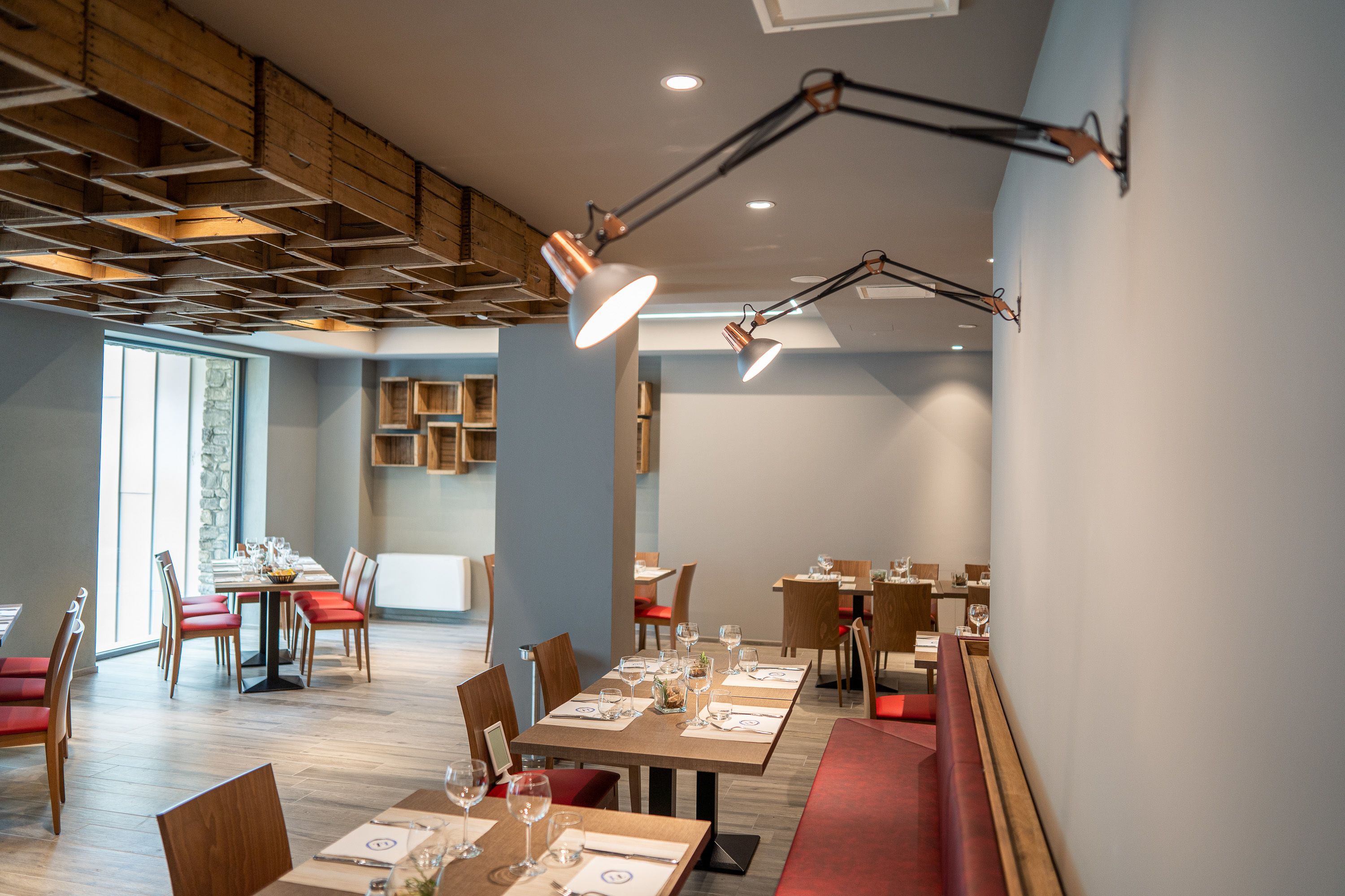 A modern dining area with wooden tables and chairs, recessed lighting, and a high ceiling with exposed beams.
