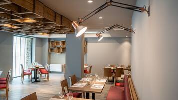 A modern dining area with wooden tables and chairs, recessed lighting, and a high ceiling with exposed beams.
