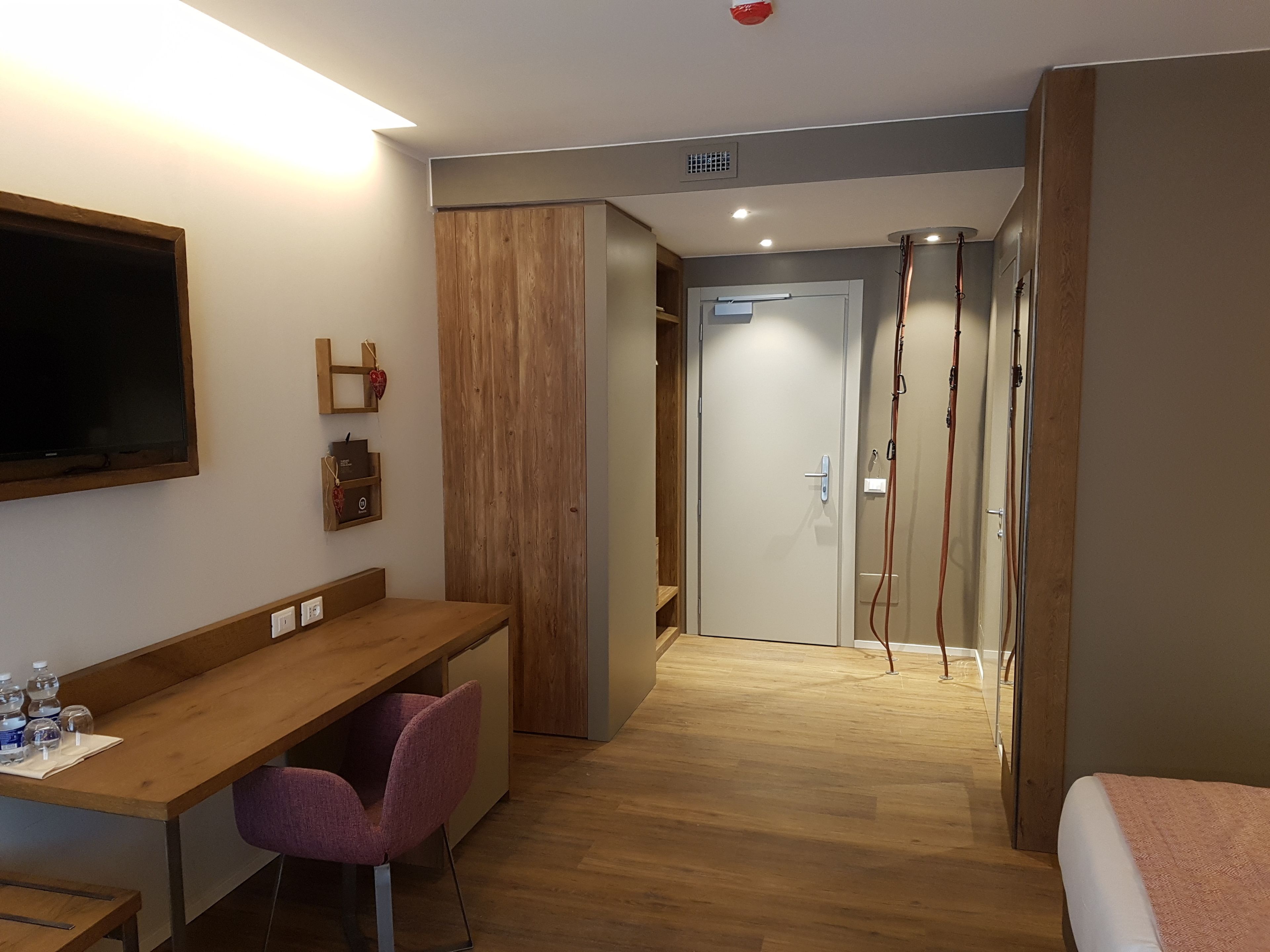 A hotel room with a wooden desk, a chair, a bed, and a TV mounted on the wall.