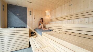 A sauna with wooden benches and a bench seat, a towel, and a bucket.