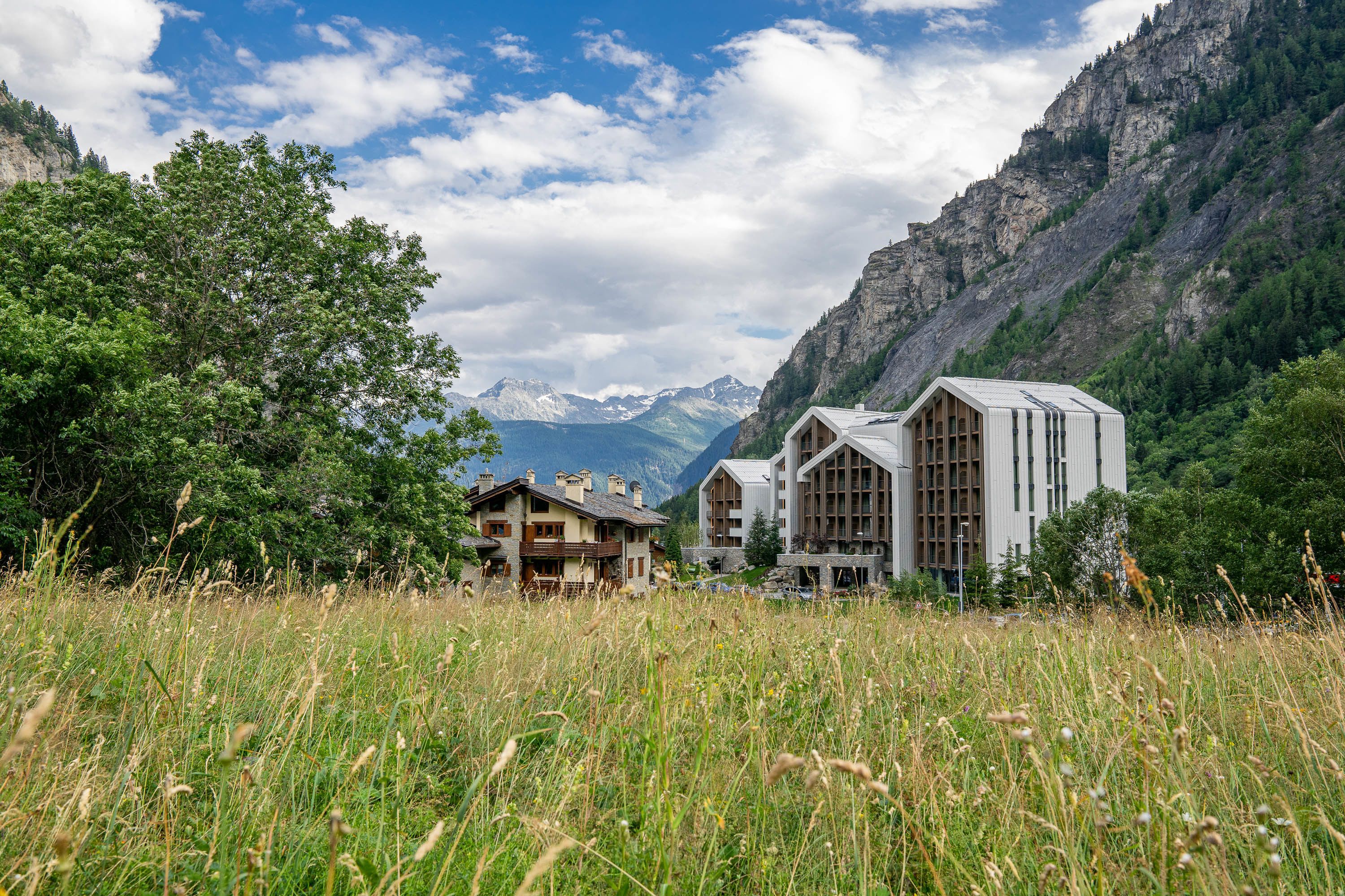 A mountain lodge with a wooden cabin and a modern building, surrounded by lush greenery and mountains.