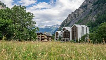 Un rifugio alpino con una baita in legno e un edificio moderno, immerso nel verde e circondato da montagne.