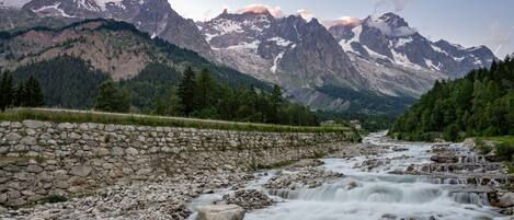 A river flowing through a rocky landscape with a stone wall on one side and a mountain range in the background.