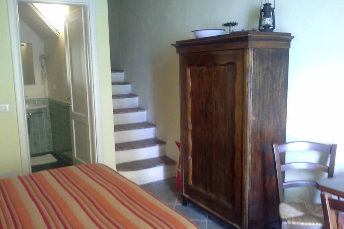 A bedroom with a bed, a wooden cabinet, a chair, and a staircase leading to another room.
