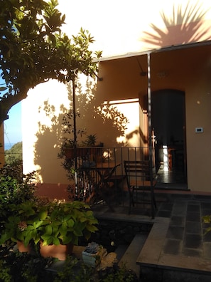 A patio area with a wooden table and chairs, surrounded by potted plants and a stone pathway. - Sole Terra Mare (Vernazza)