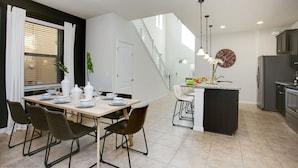 A modern kitchen with a central island, a dining area with a table set for four, and a staircase leading to an upper level.