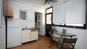 Una cocina compacta con refrigerador, alacenas, una mesa de comedor con sillas, un ventilador de techo y una ventana con persianas.