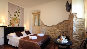 Una habitación de hotel con una cama, una mesa con una vela y una pared de piedra.