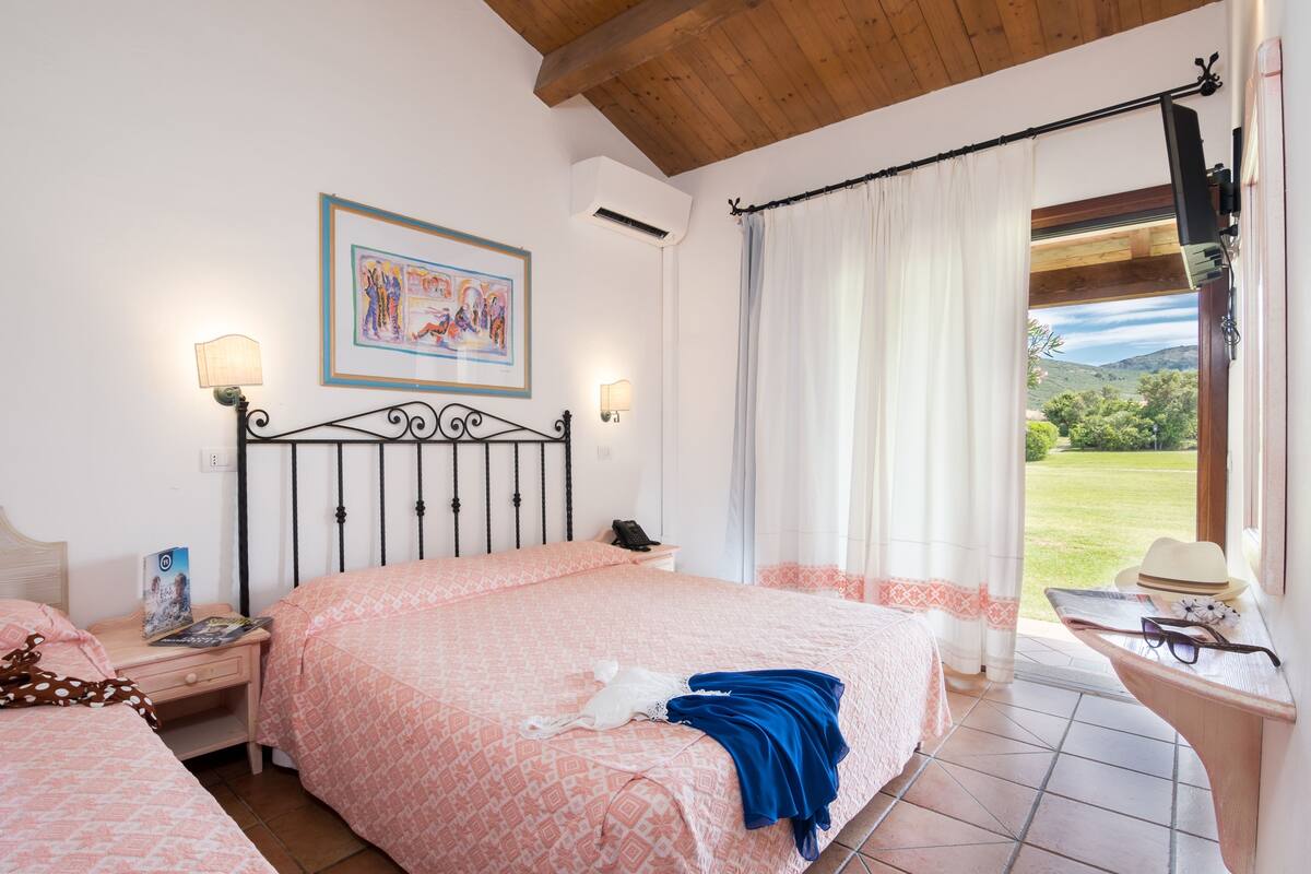 Een slaapkamer met een bed, nachtkastjes, gordijnen voor het raam en uitzicht op de omgeving.