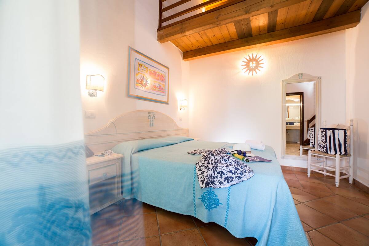 Een slaapkamer met een bed, nachtkastjes, een spiegel en een deur naar een andere kamer.