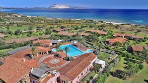 Un complexe hôtelier doté d’une piscine centrale, de toits en terrasses et offrant une vue sur la mer et une montagne en arrière-plan.