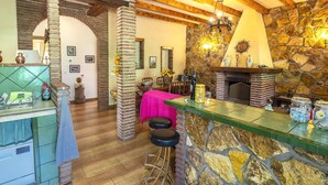A rustic interior with exposed wooden beams, a stone fireplace, and a bar area with stools.