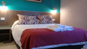 Un lit bien fait, avec une couverture rouge et des oreillers blancs, une table de chevet avec une lampe et un tableau accroché au mur.