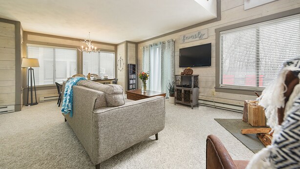 A spacious living room with a high ceiling, a fireplace, a television, and a dining area with a table and chairs.