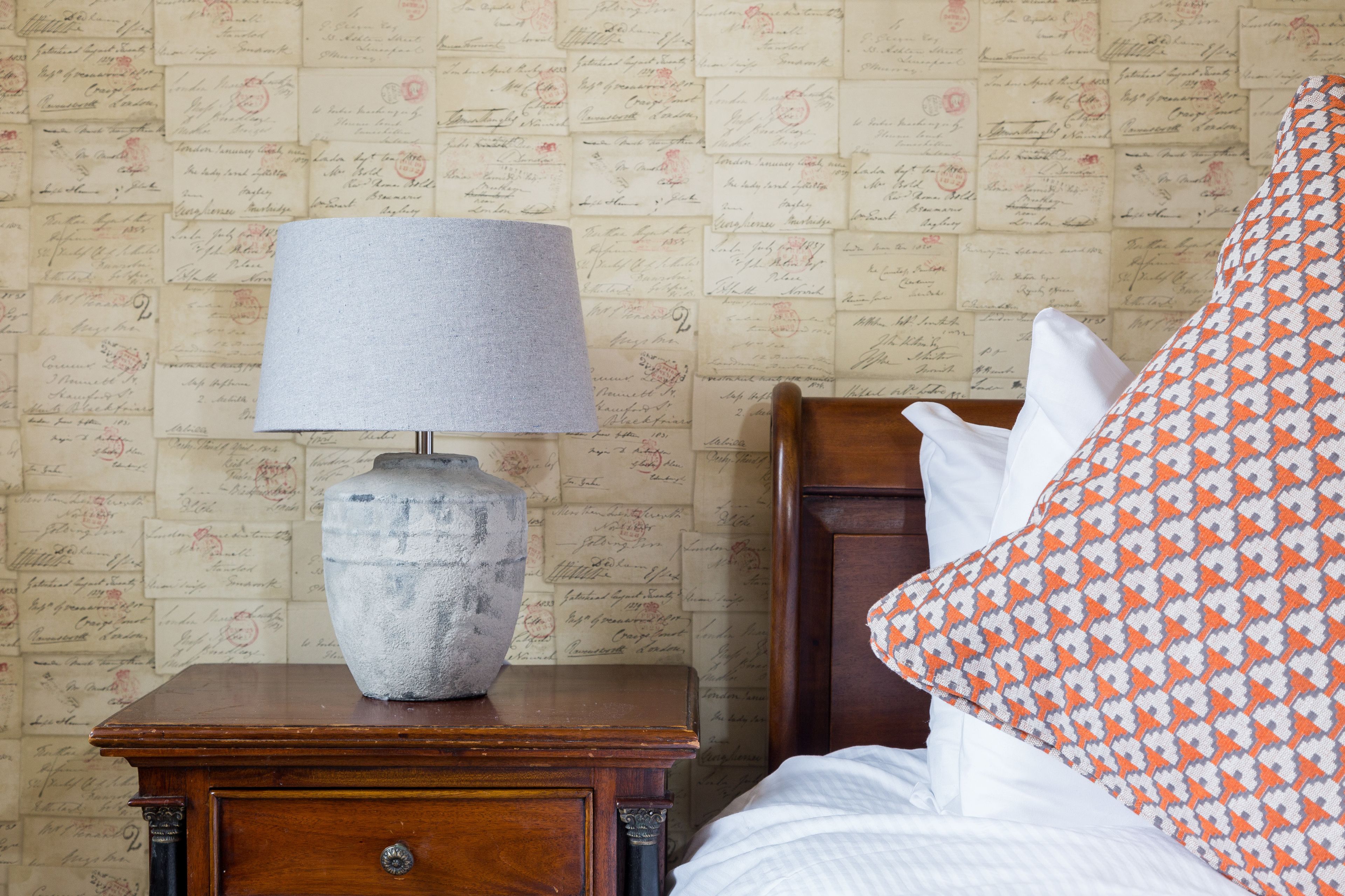 A wooden nightstand with a lamp and a wall covered in vintage postcards.