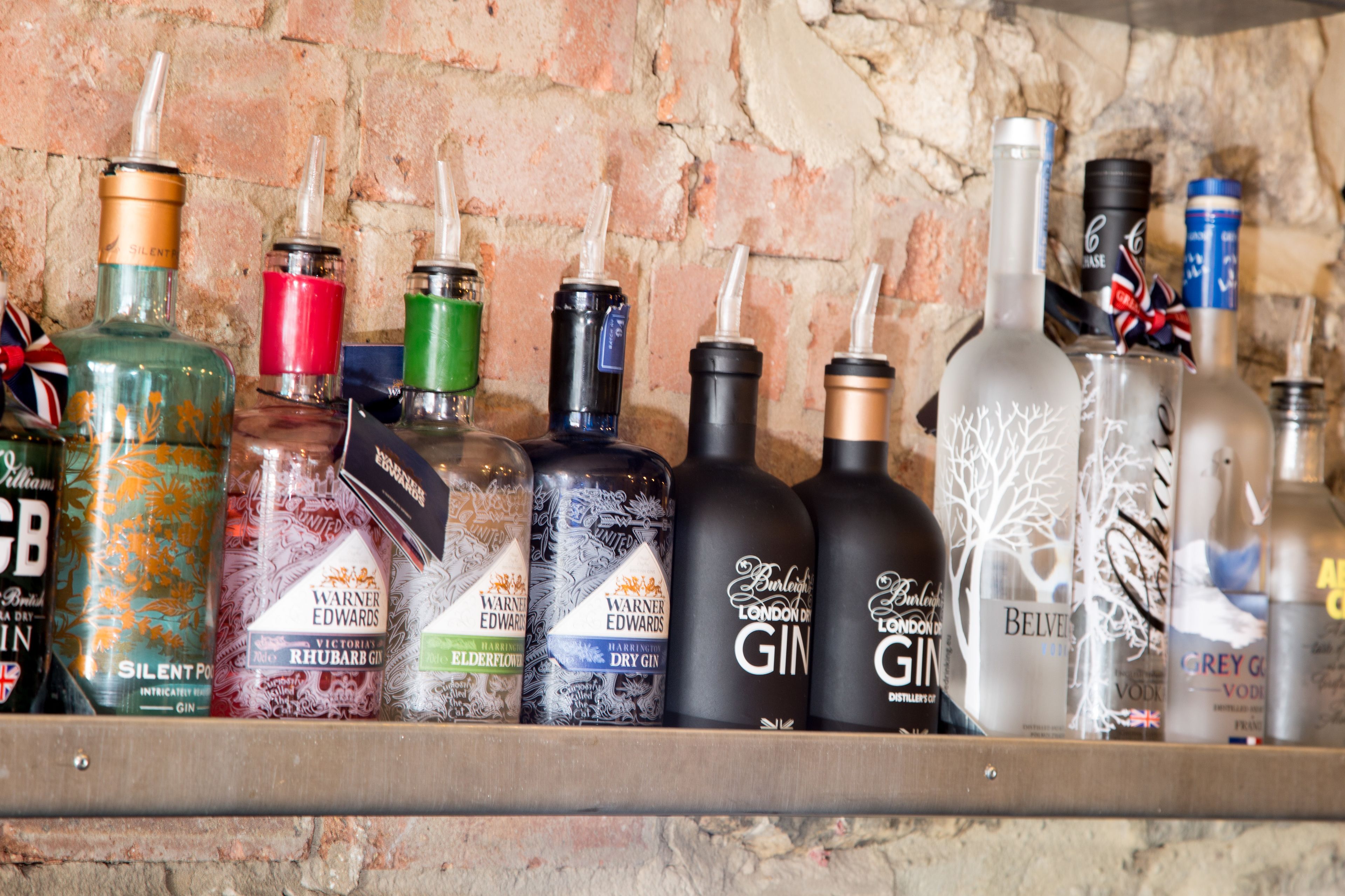 A variety of gin bottles on a shelf against a brick wall.