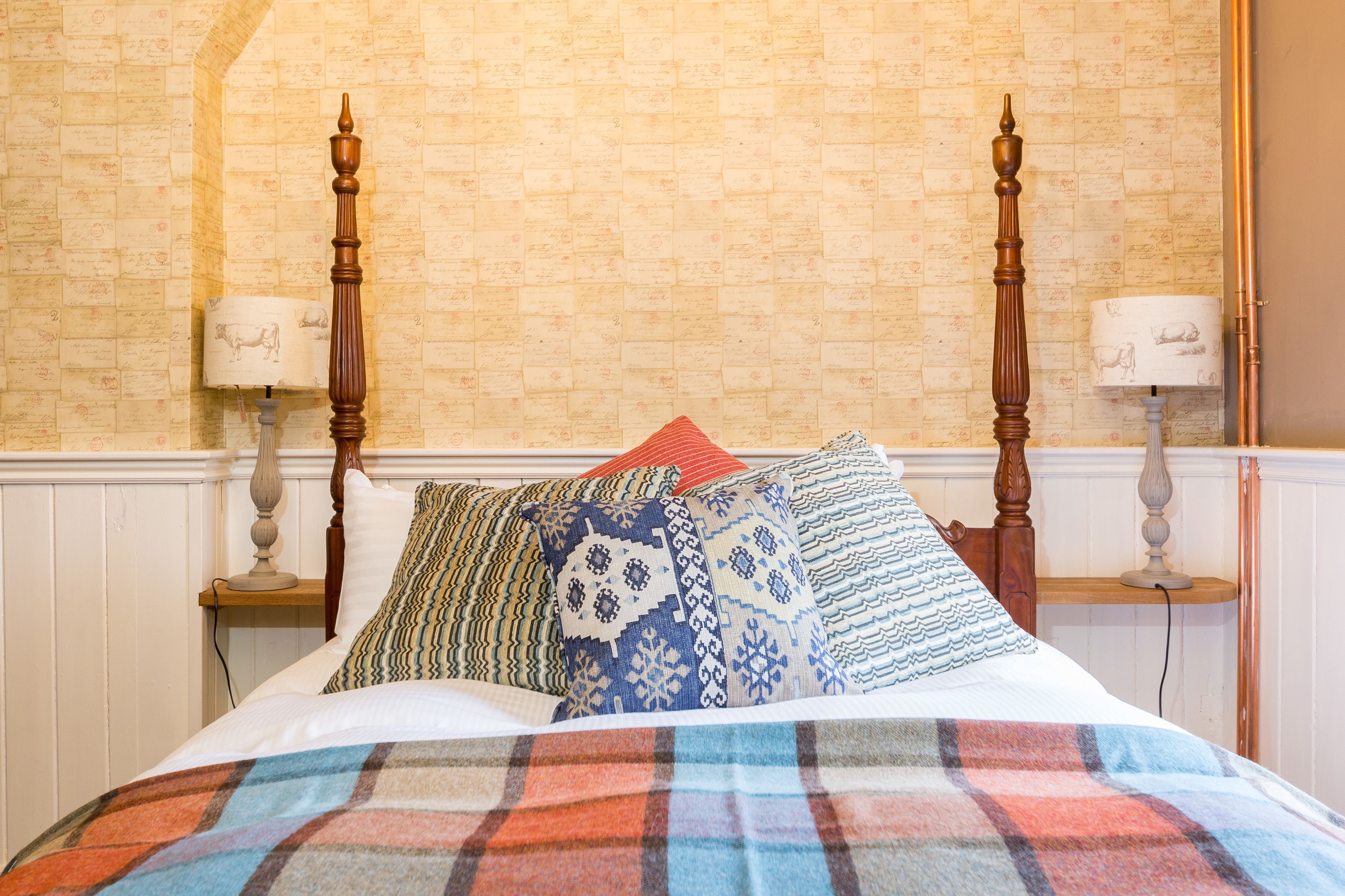 A neatly made bed with patterned pillows and a plaid blanket, a wooden headboard, and two bedside lamps with animal-themed lampshades.