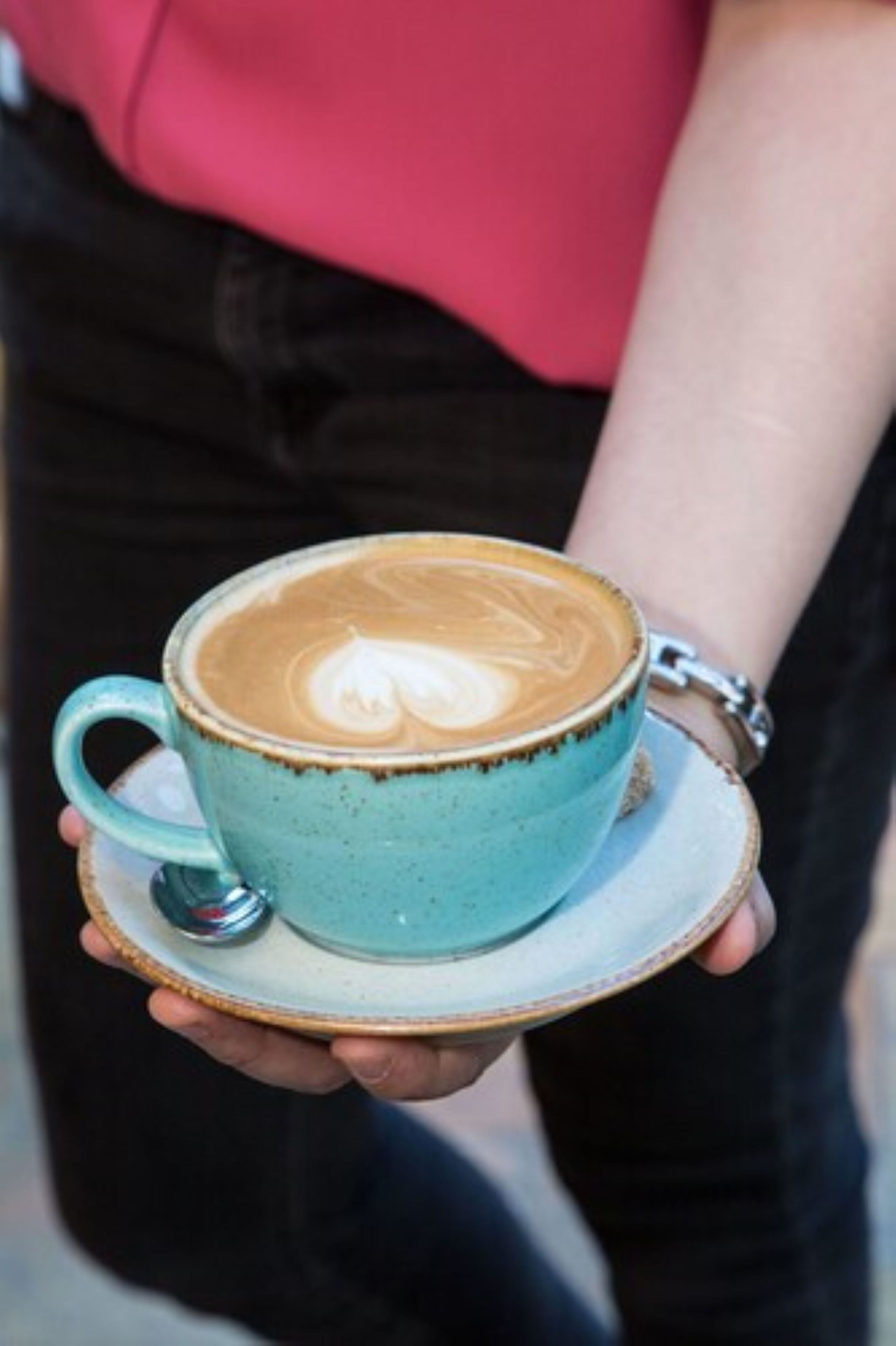 A person holding a blue ceramic cup with latte art on a saucer.