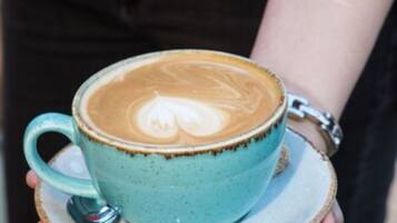 A person holding a blue ceramic cup with latte art on a saucer.