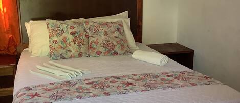A neatly made bed with floral bedding, a wooden headboard, and a painting of a surfer on the wall.