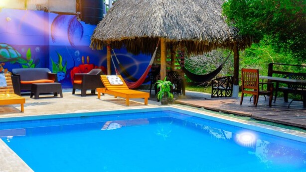 A swimming pool with lounge chairs, a hammock, and a thatched-roof structure. - Posada Luna (Tamanique)