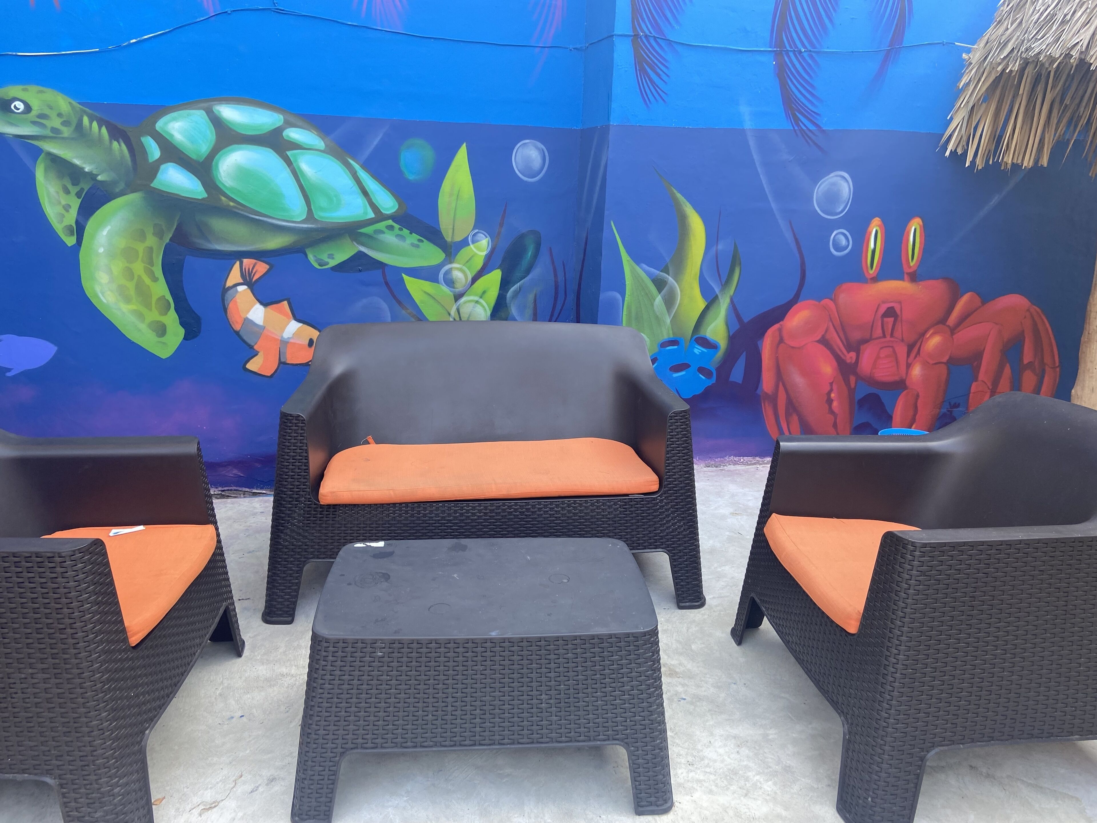 A seating area with wicker furniture and orange cushions, set against a mural of an underwater scene with a turtle and other sea creatures.