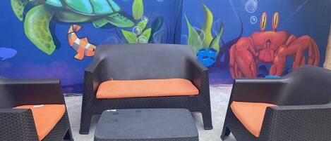 A seating area with wicker furniture and orange cushions, set against a mural of an underwater scene with a turtle and other sea creatures.