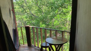 A balcony with a wooden table and chairs, a rope, and a view of green foliage. - Posada Luna (Tamanique)