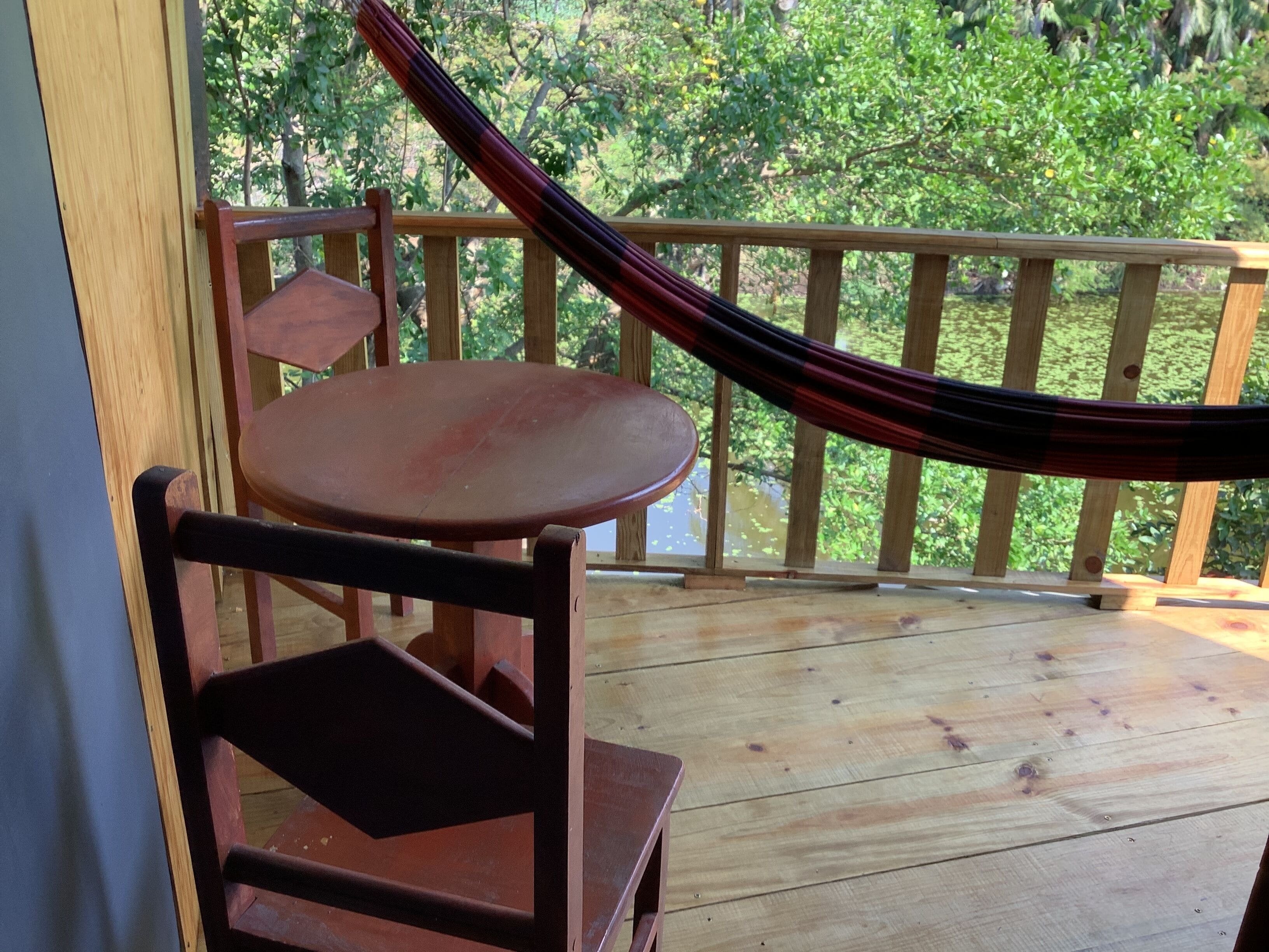 Une terrasse en bois avec un hamac, une chaise en bois et une petite table.