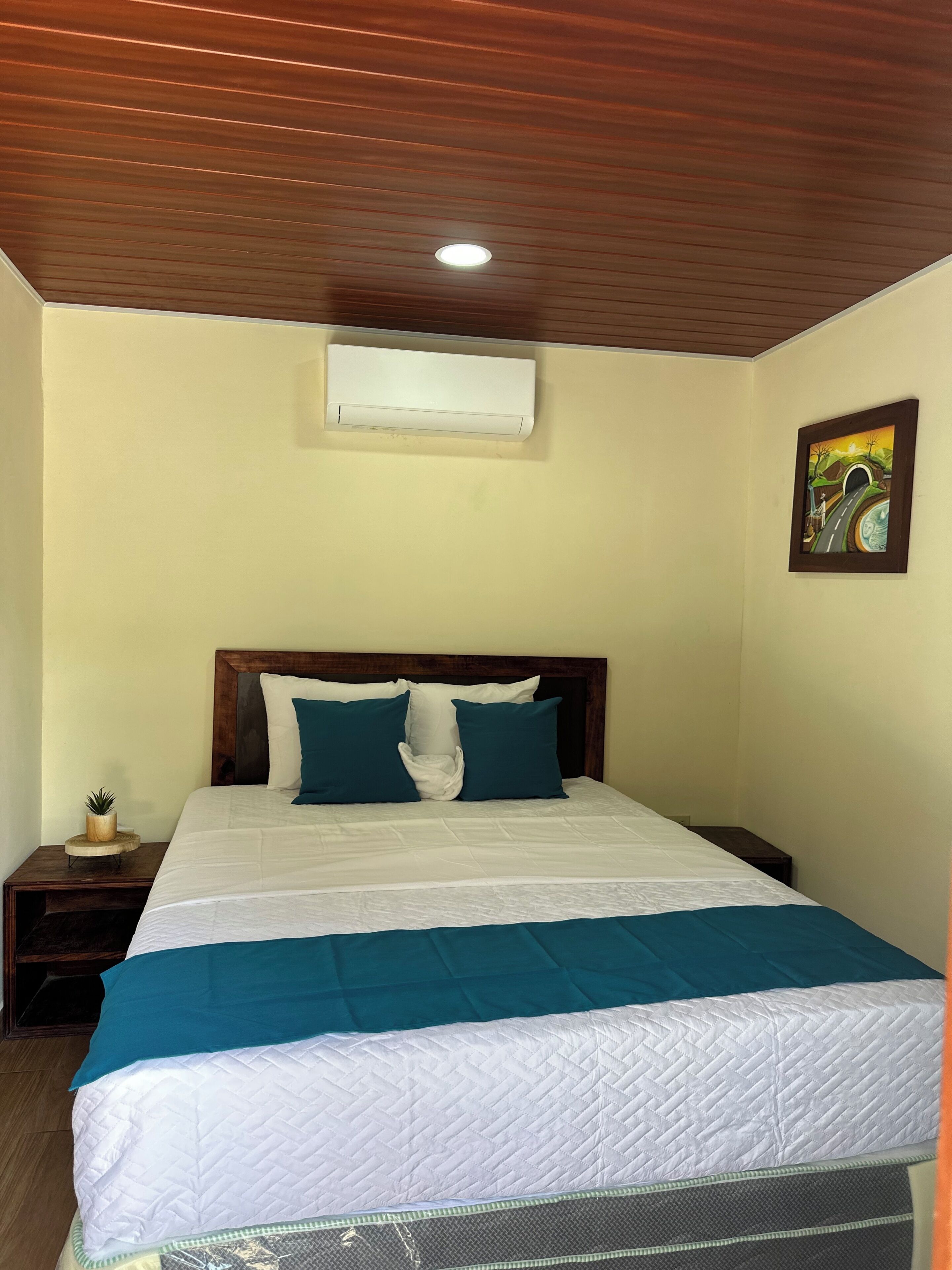 A bedroom with a bed, a nightstand, a wall-mounted air conditioner, and a painting.