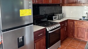 A kitchen with stainless steel appliances, wooden cabinets, and a tiled floor. - Posada Luna (Tamanique)