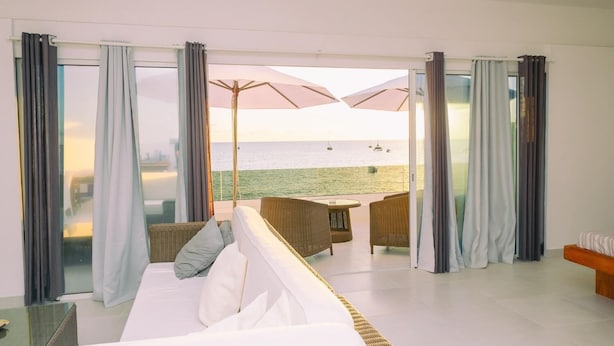 A room with a white sofa, wicker chairs, and a view of the sea. - Etoile Blanche (Nosy Be)