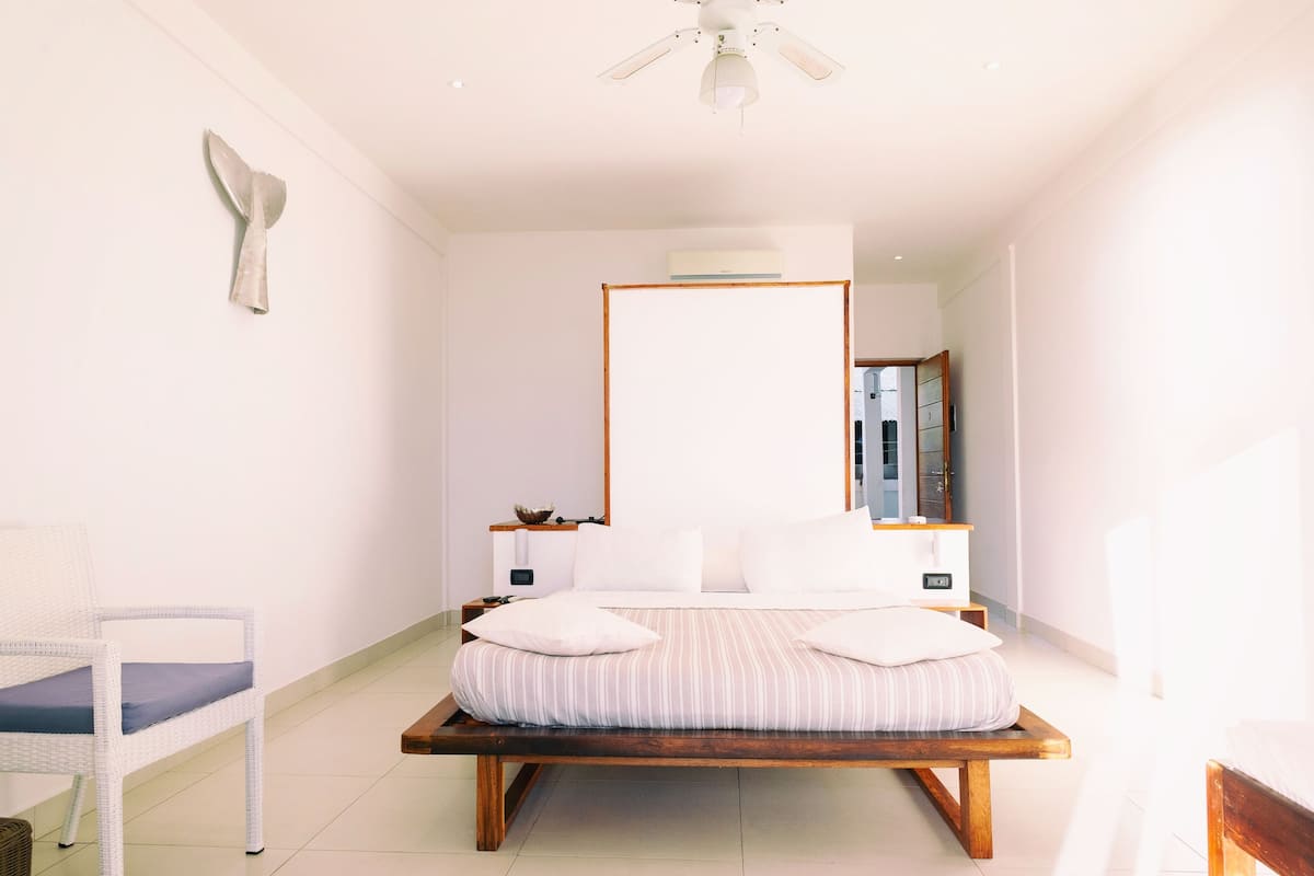 A minimalist bedroom with a bed, a chair, and a ceiling fan.