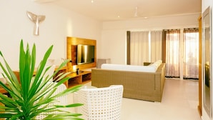 A modern hotel room with a large bed, a TV mounted on a wooden panel, a white chair, and a potted plant. - Etoile Blanche (Nosy Be)