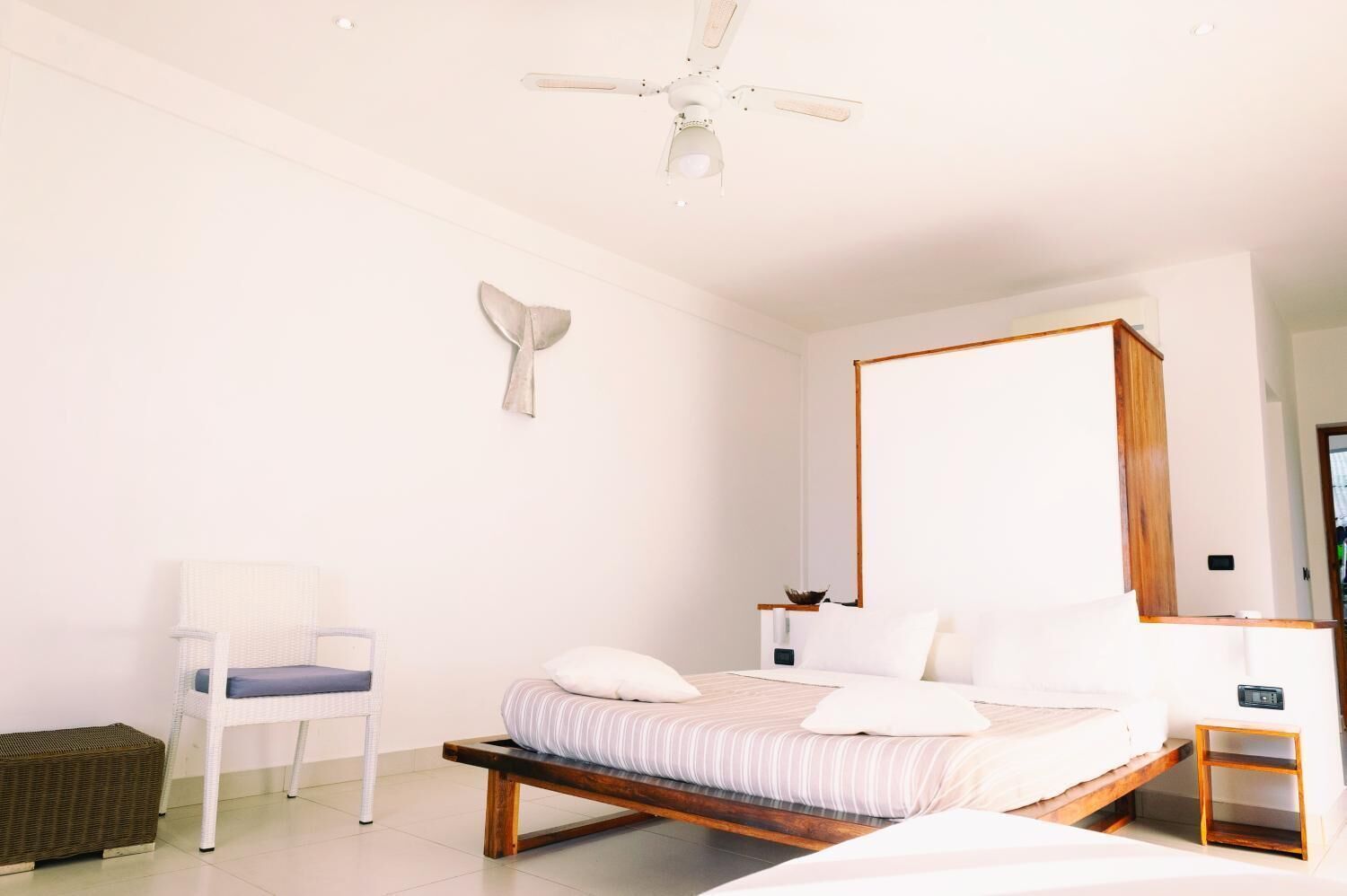 A minimalist bedroom with a bed, a chair, and a ceiling fan.
