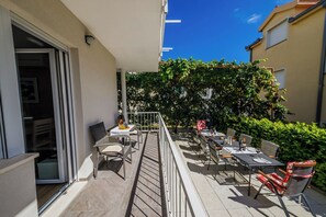 Un balcon avec des sièges d’extérieur, une table avec une bouteille, et une vue sur un immeuble avec un ciel bleu.