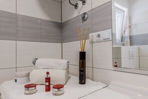 Une salle de bain moderne avec un lavabo blanc, un miroir et des articles de toilette, notamment un flacon de lotion, un pot de crème et un flacon de parfum.
