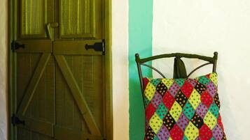A chair with a colorful quilted pillow against a wall with a green door.
