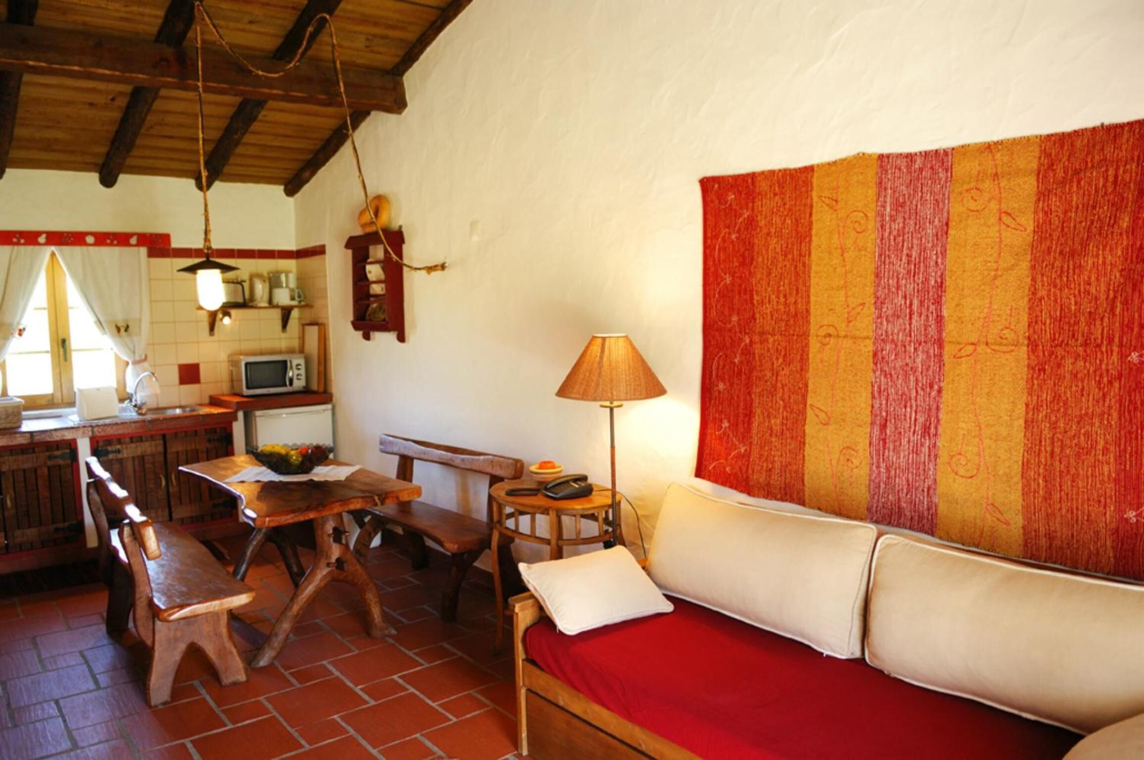 Una habitación acogedora con un banco de madera, una mesita, un sofá con una manta roja, una lámpara y un microondas.