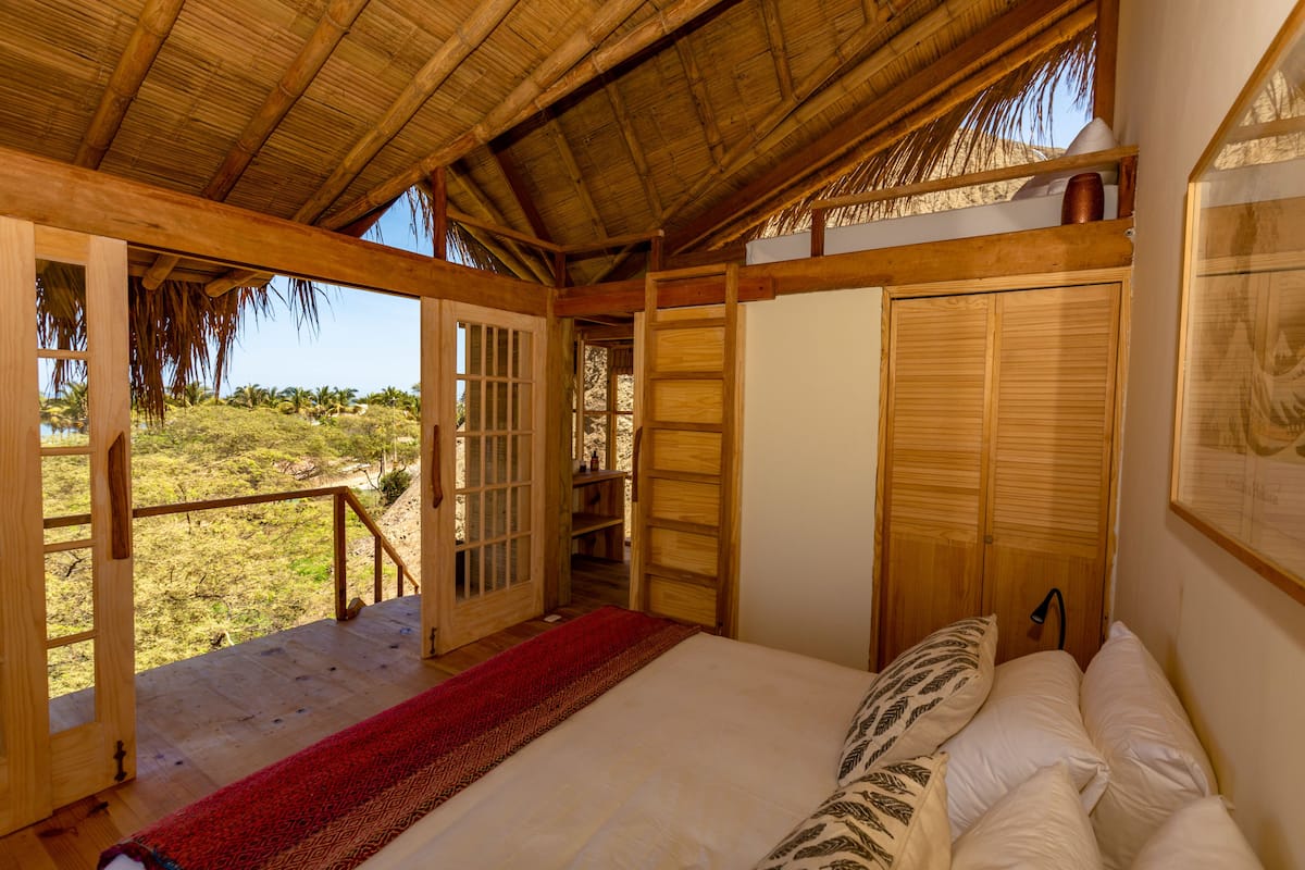 Una habitación con una cama, puertas de madera, un tapete rojo y vistas al exterior.