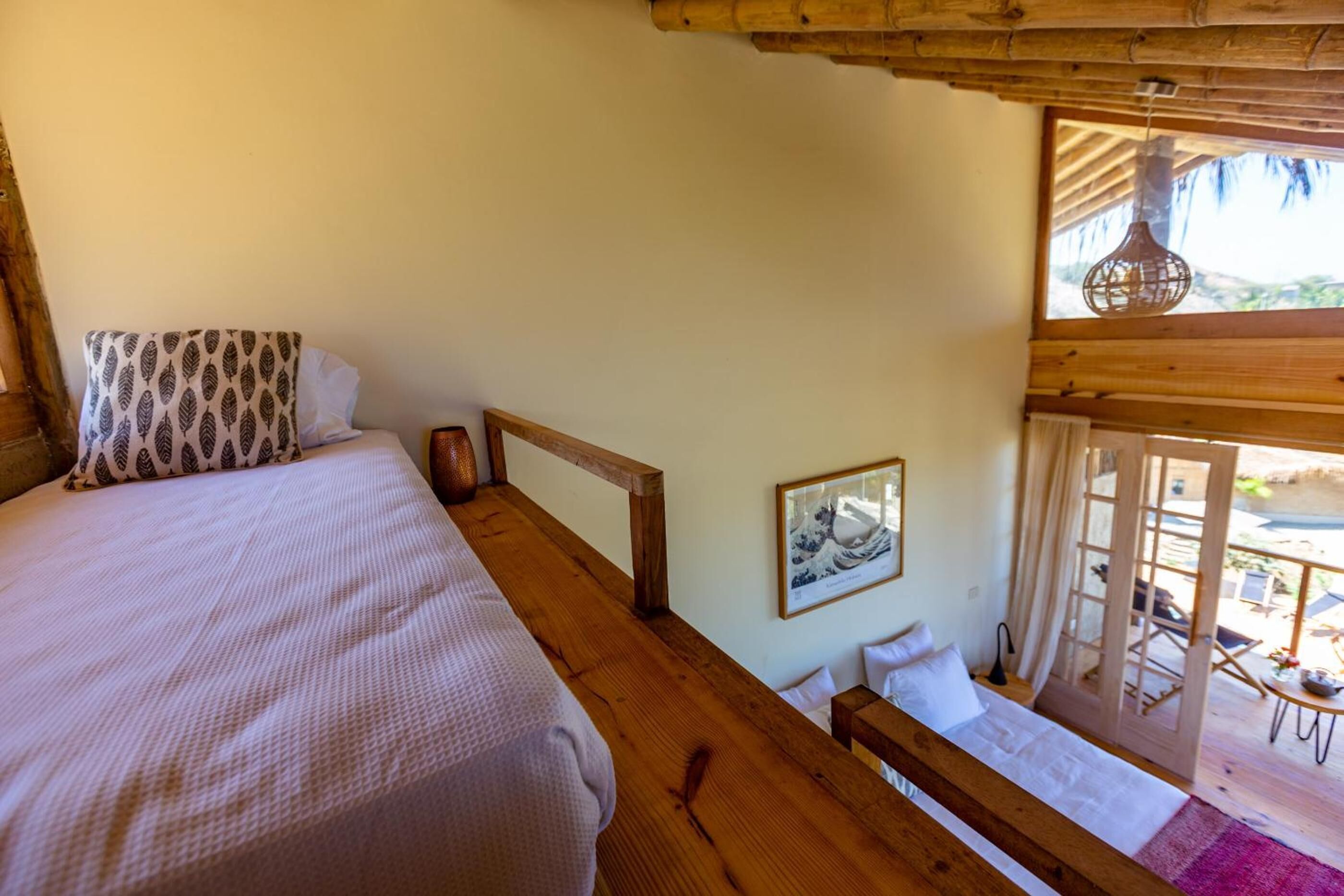 A bedroom with a large bed, wooden ceiling, and a balcony with a view.